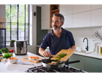 Um homem cozinhando em uma cozinha moderna, adicionando ervas a uma panela em um fogão a gás.
