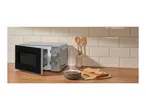 Microwave oven with an open door, a bowl of soup, and sliced bread on a wooden counter.