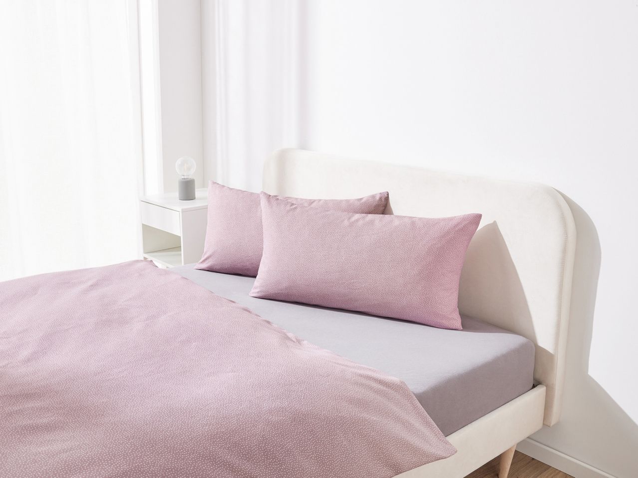 A bed with pink polka dot duvet cover and pillows, and a grey fitted sheet.