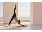 Woman in CRIVIT sports leggings and yoga top on a terrace with a sea view.