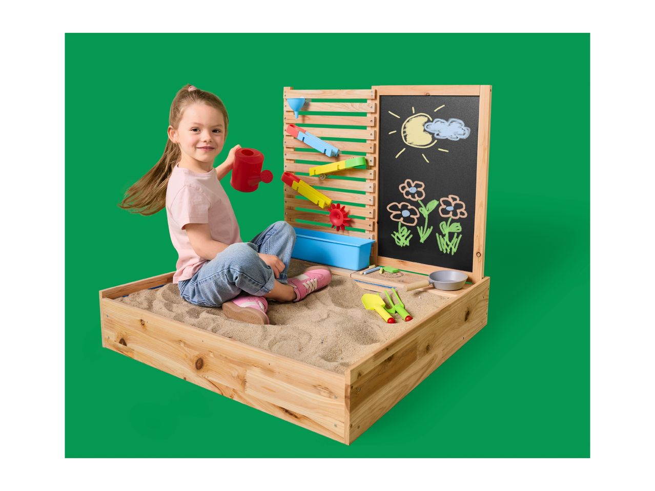 Girl playing in a wooden sandpit with a water wall and chalkboard with drawings.