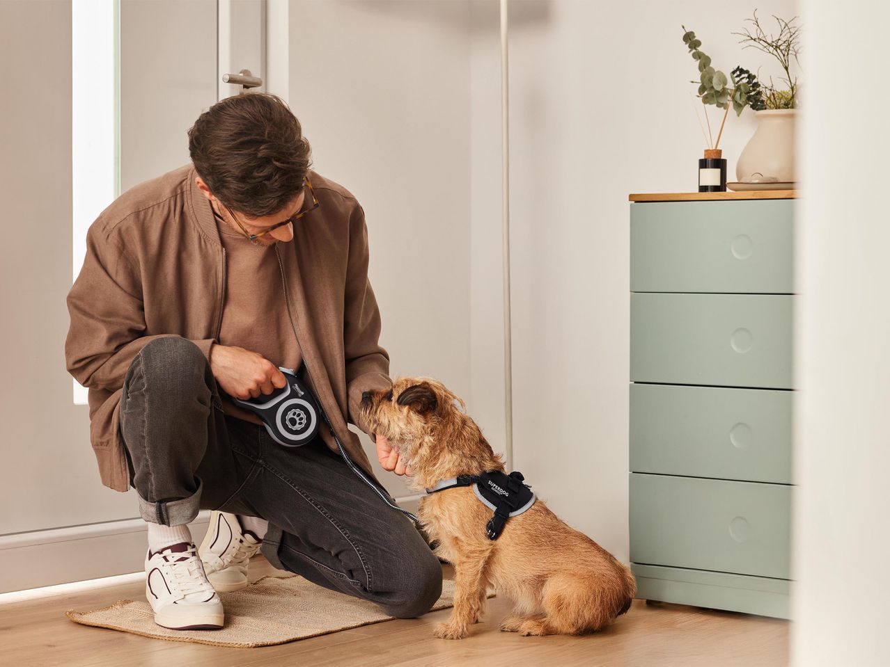 Egy férfi kutyát sétáltat, flexi pórázzal és Superdog hámban.