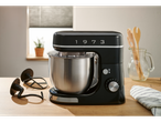 Black stand mixer with a stainless steel bowl and attachments on a wooden counter.