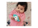 Baby in a pink romper lying on a rug, holding a hedgehog-shaped teether.