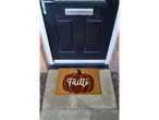 A pumpkin-themed doormat with 'Fàilte' written on it, placed in front of a black door.