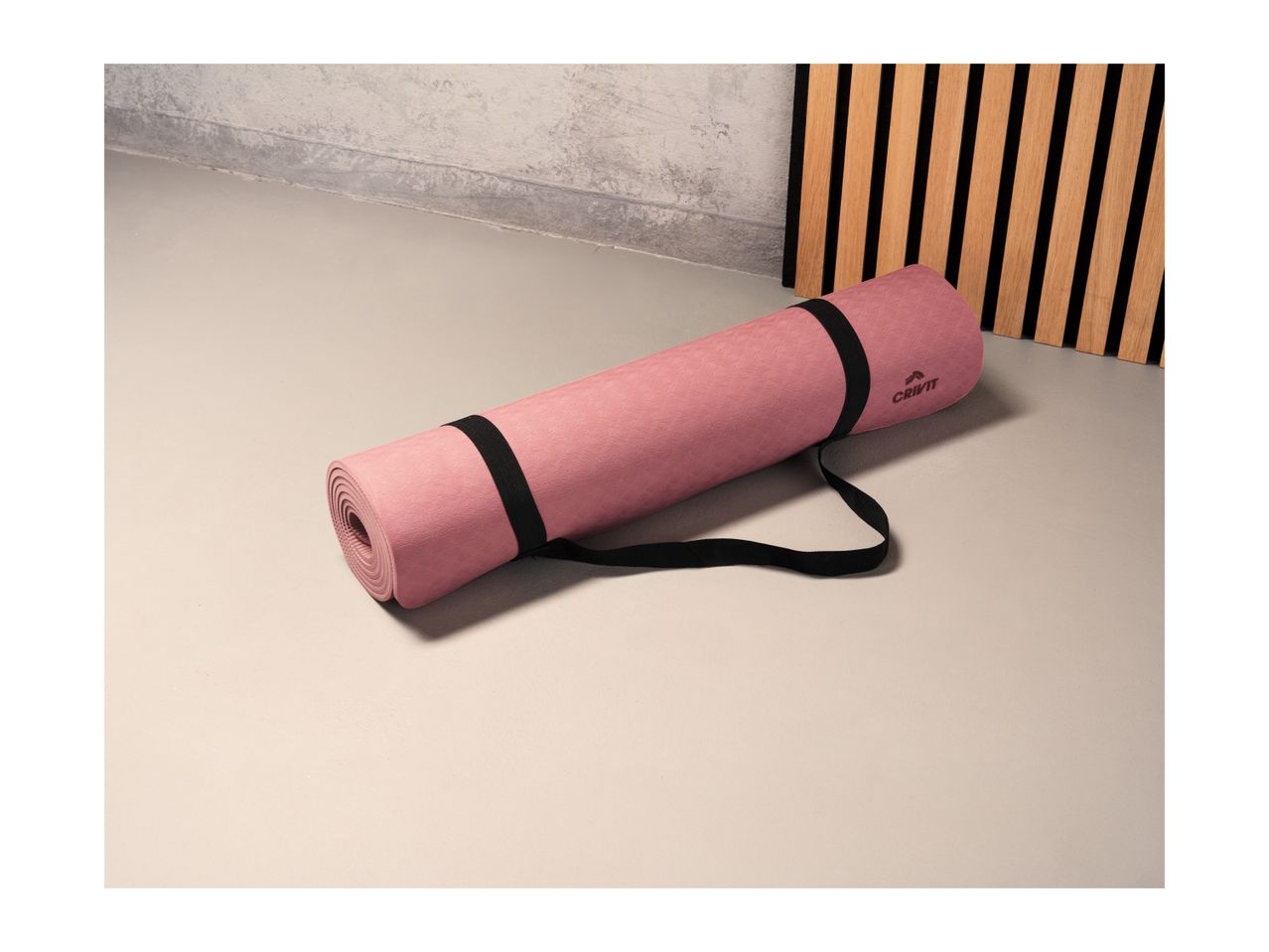 Pink Crivit yoga mat with a black strap on a light floor.
