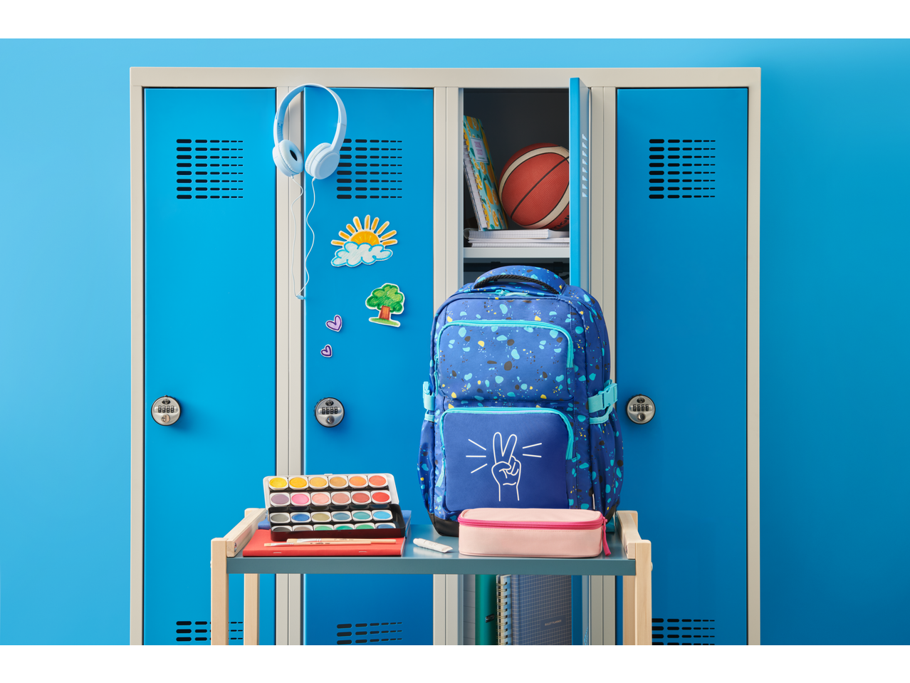 Armário escolar azul com mochila, material de pintura e bola de basquetebol, pronto para a escola.