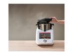 A person lifting the lid of a Monsieur Cuisine Smart food processor, with steam rising.