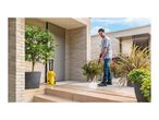 Man pressure washing a patio with a yellow pressure washer, surrounded by potted plants.
