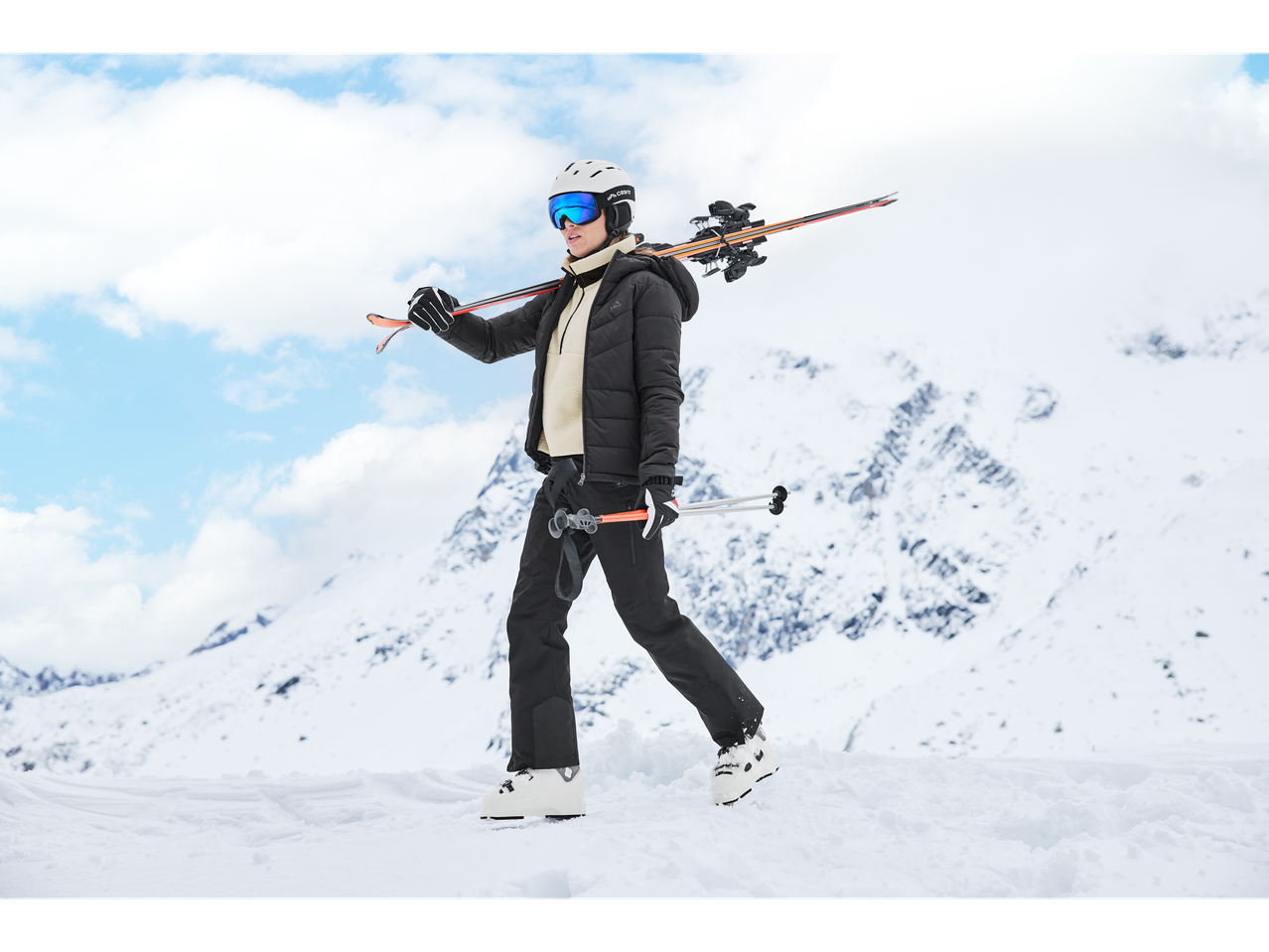 Woman in Crivit ski jacket, pants, and goggles, carrying skis on her shoulder