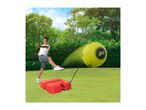 Boy kicking a yellow tethered football on a red base in a grassy garden.