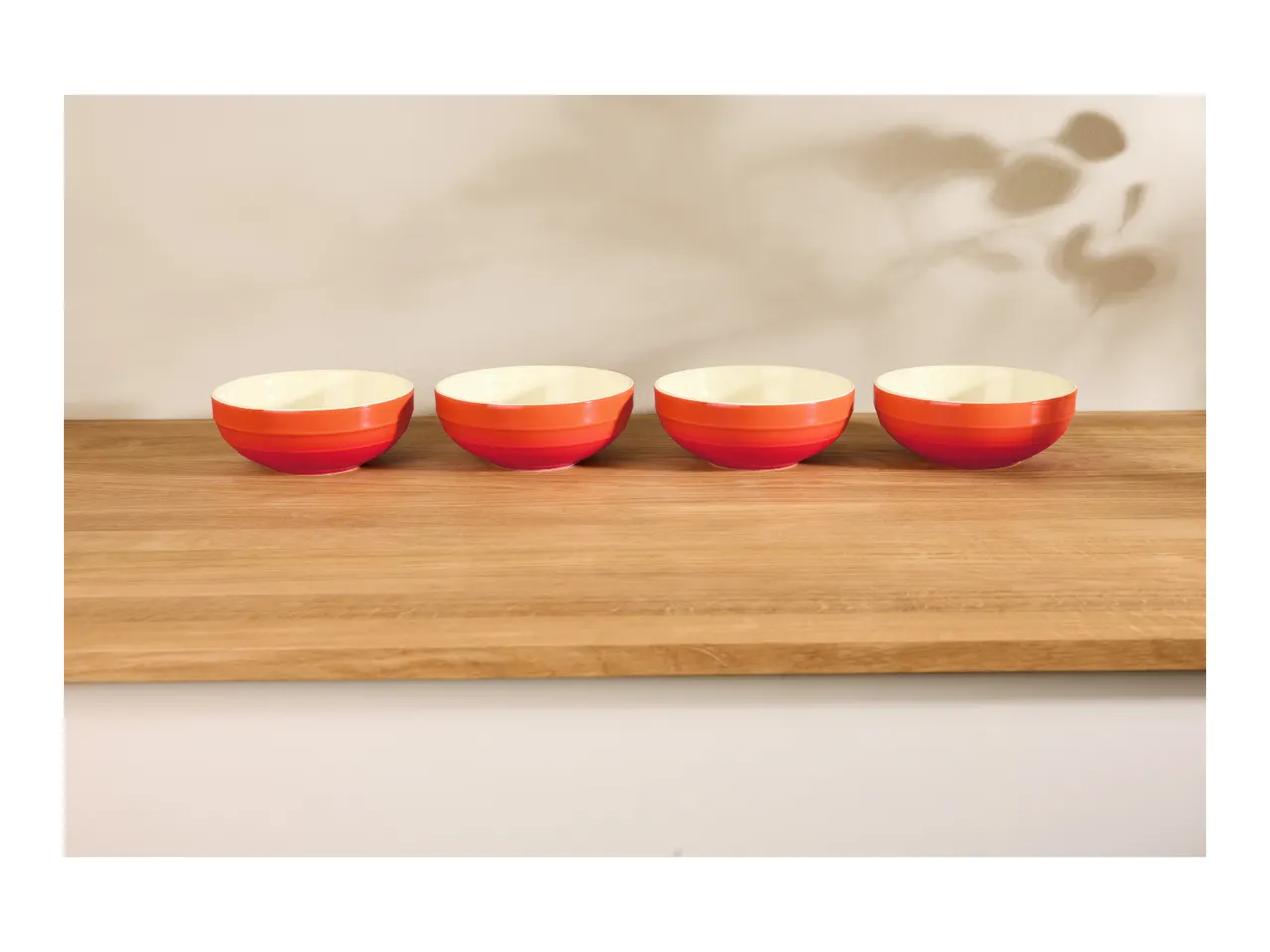 Four red and orange gradient bowls on a wooden surface with plant shadows on the wall.