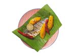 Grilled fish fillet with mango, chili, and lime on a banana leaf, served on a patterned plate.