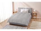 A light grey quilted bedspread on a grey upholstered bed in a bright bedroom.