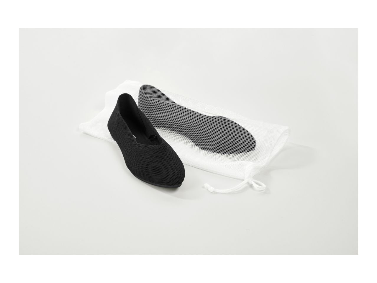 Black ballet flats with a white mesh laundry bag on a white background.
