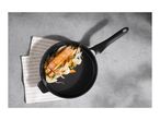 Salmon fillet with vegetables in a black frying pan on a concrete surface with a striped towel.