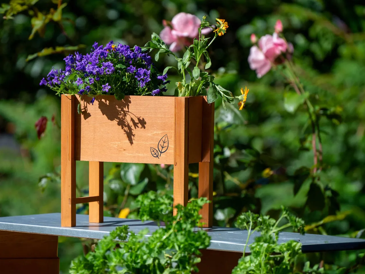Wooden planter box with purple and orange flowers, set against a green garden.
