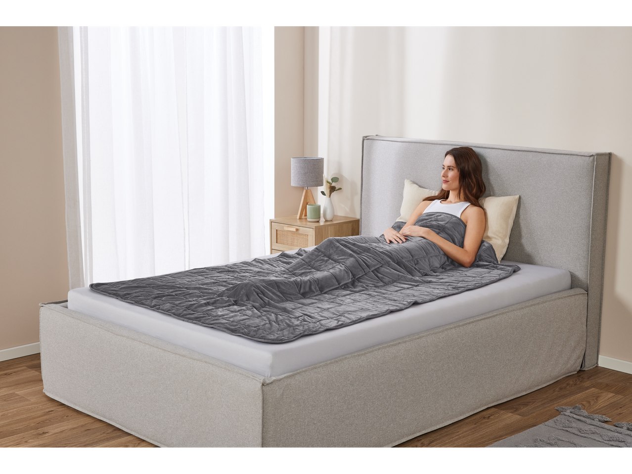 Relaxed woman on bed, covered with a gray blanket.