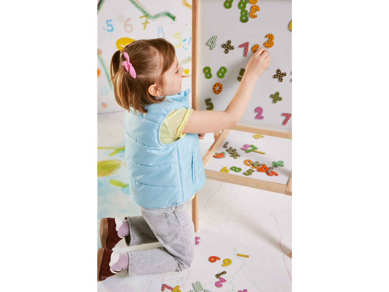 Criança brincando com números magnéticos em um quadro branco.