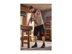 Man in work shorts and t-shirt drilling wood on a workbench in a workshop.
