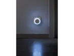 A white circular night light plugged into a wall socket, illuminating the floor.