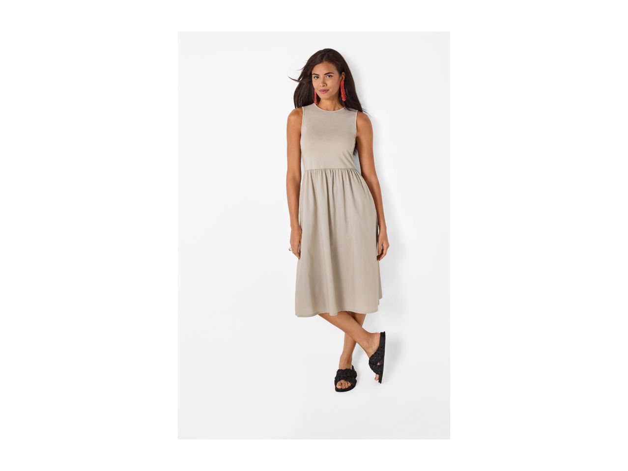 Woman in a beige sleeveless midi dress and black sandals, posing with one leg crossed.