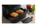 Black air fryer with two whole roasted chickens inside, surrounded by fresh bell peppers and tomatoes.