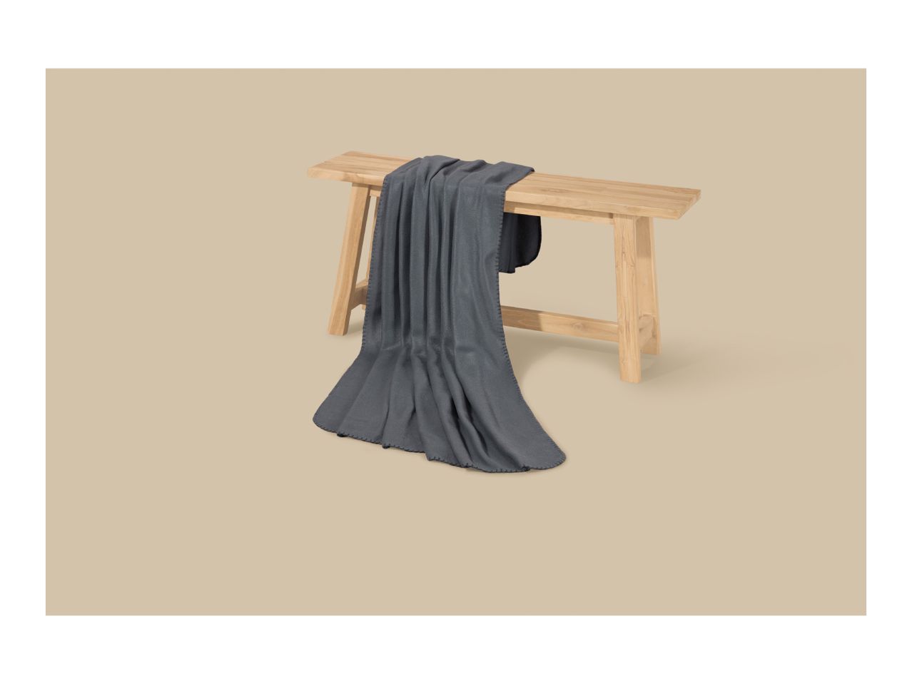 Dark grey blanket draped over a light wooden bench on a beige background.