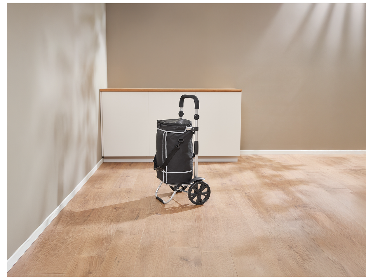 Un chariot de courses noir avec des bandes réfléchissantes dans une pièce vide avec un sol en bois.