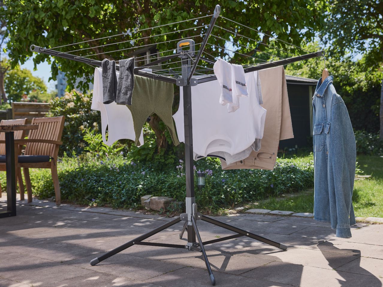 A black rotary clothesline with various clothes drying on a patio.