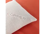 A Copper brand pillow with a textured, breathable cover rests on a burnt orange surface.