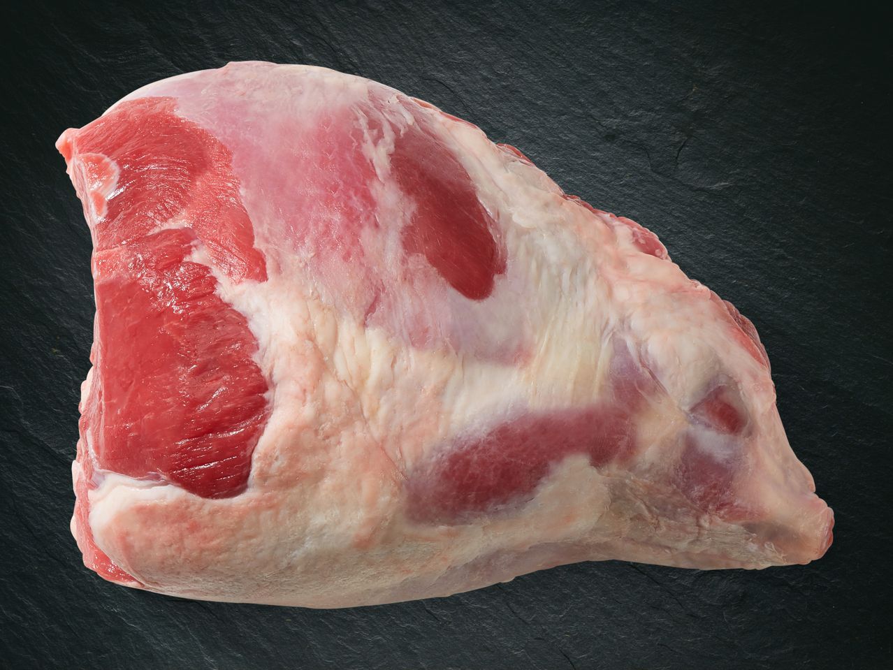 Un taglio di carne di agnello crudo su una superficie scura.