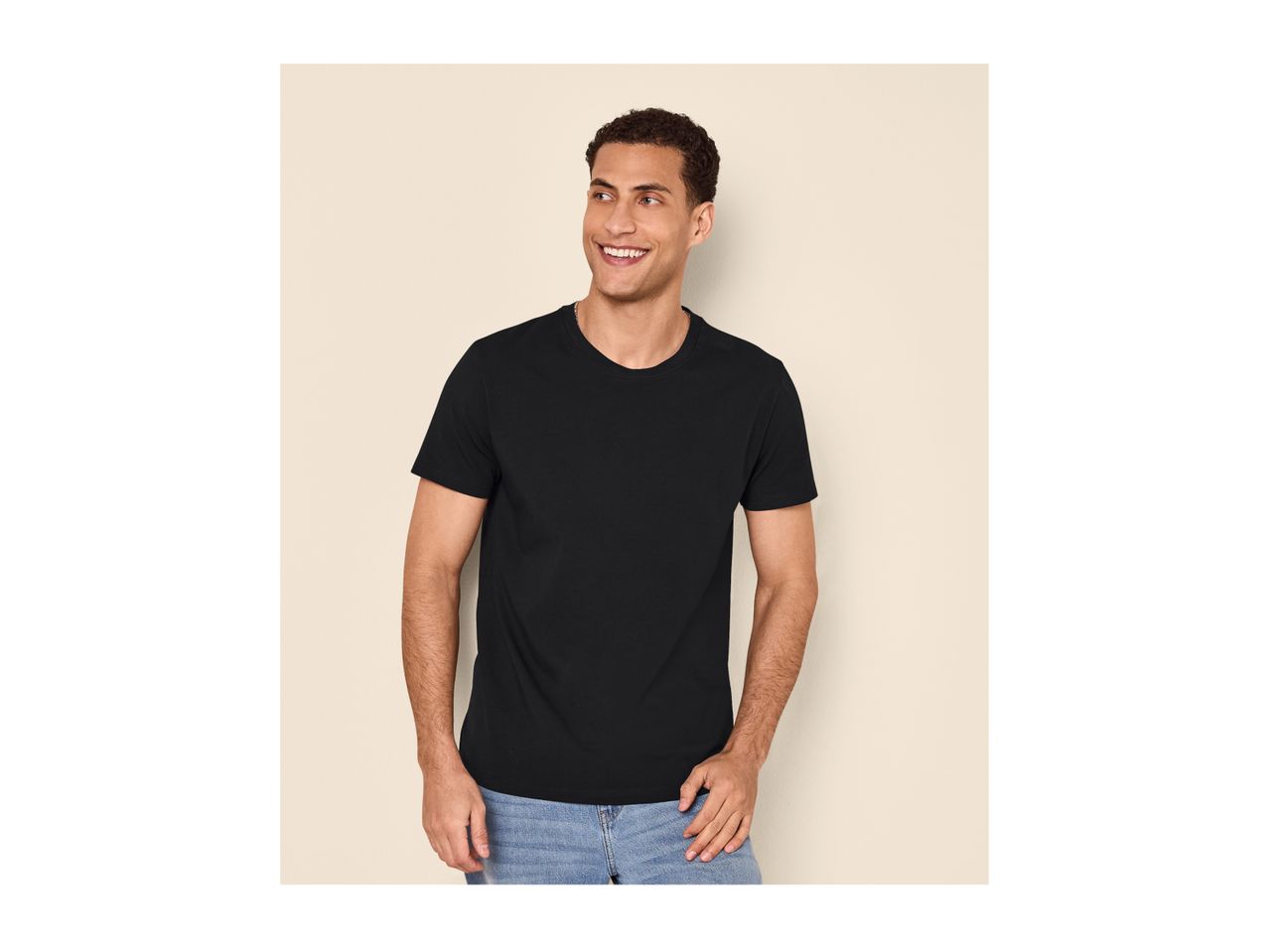 A man in a black t-shirt and blue jeans smiles while looking to the side.