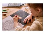 Child scratching a colorful phoenix design on a scratch art book, with a mandala coloring page nearby.