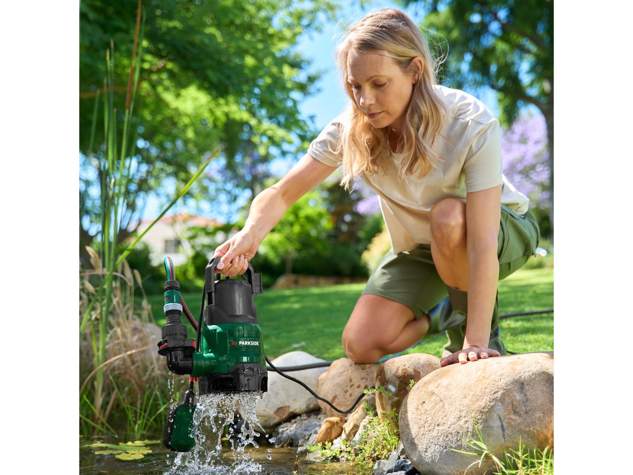 Woman placing a submersible pump into a pond, with water splashing.