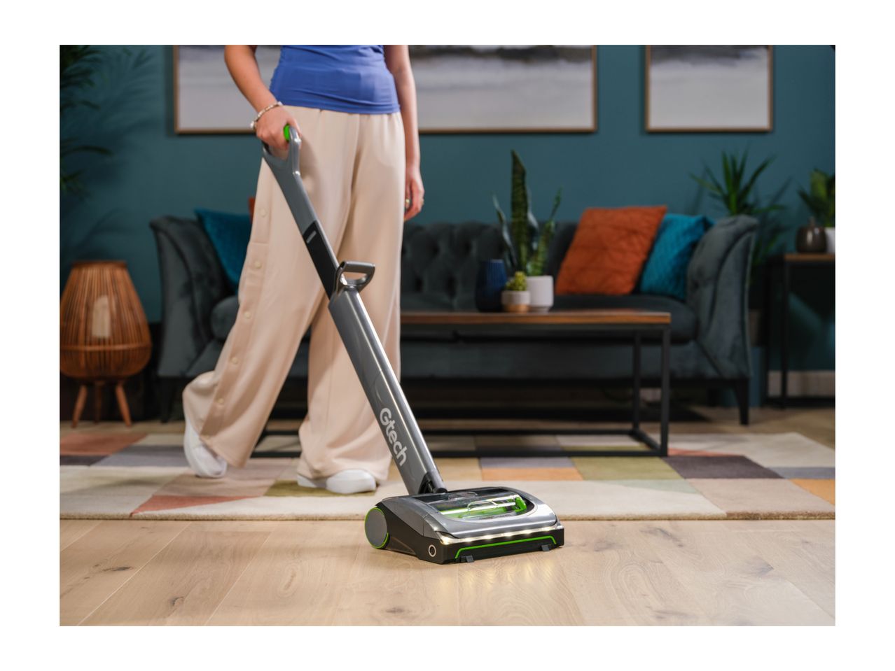 A person using a cordless floor cleaner on a wooden floor in a living room.