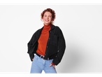 Woman in a black corduroy jacket, orange turtleneck, and light blue jeans