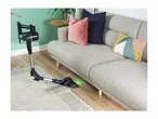 Cordless stick vacuum cleaner cleaning under a grey sofa with colorful cushions.