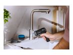 A person cleaning a kitchen sink and faucet with a black electric cleaning brush.
