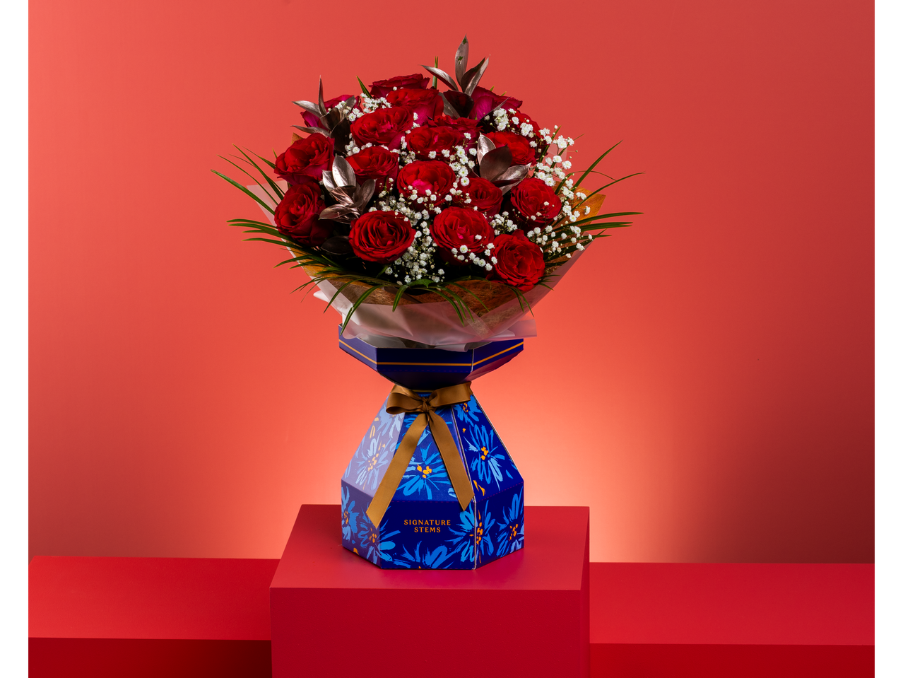 Red rose bouquet with baby's breath in a blue floral box, on red platforms.