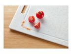 Fresh tomatoes, one whole and two halves, with tomato juice on a white cutting board.