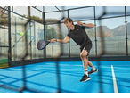 Homem de roupa desportiva preta a jogar padel num campo azul com uma raquete.