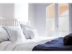 Cama com roupa de cama branca e almofadas com detalhes azuis.