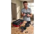 Man inserting a drill bit into a cordless drill, with a tool case and bit sets on a wooden surface.