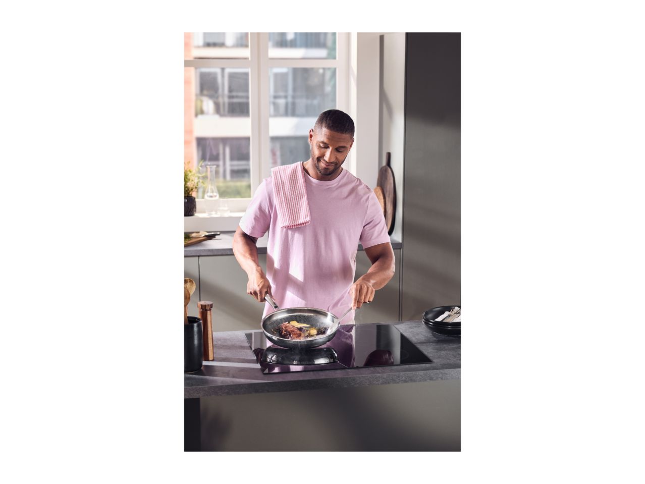Man cooking steak and vegetables in a frying pan on an induction hob in a modern kitchen.