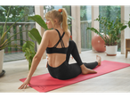 Mulher de sutiã desportivo Crivit preto e leggings, a fazer ioga num tapete.