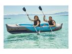 Two people in an inflatable kayak on clear blue water, paddling and smiling.