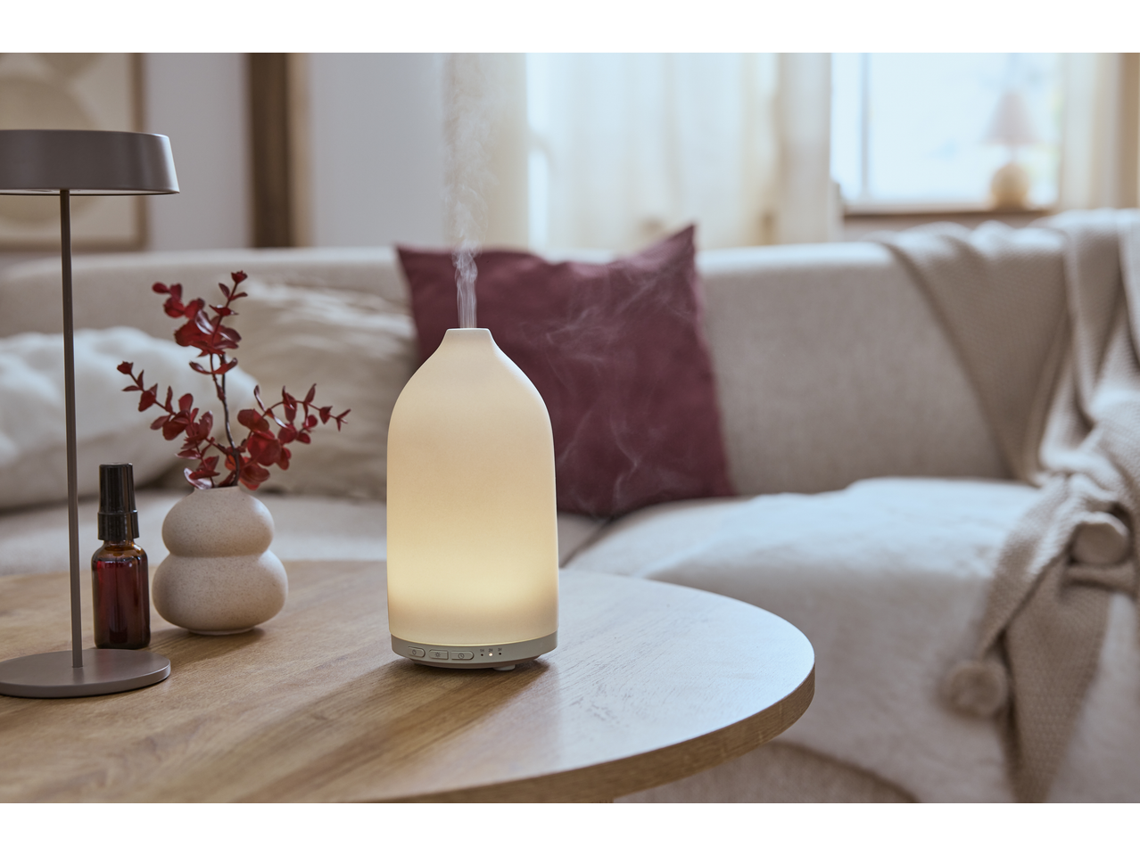 A glowing aroma diffuser emitting mist on a wooden table, with a sofa in the background.