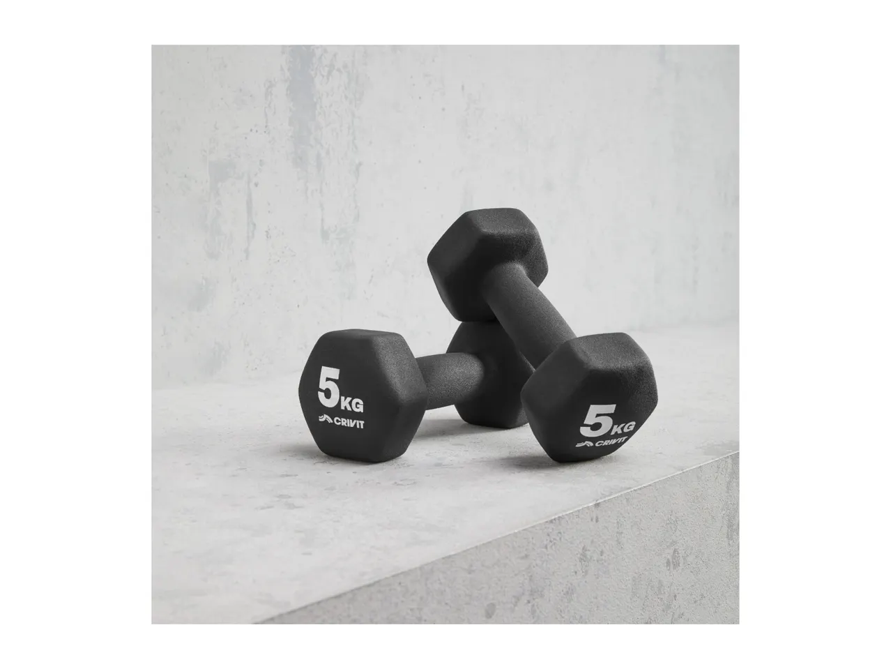 Two black 5kg Crivit dumbbells on a concrete surface.