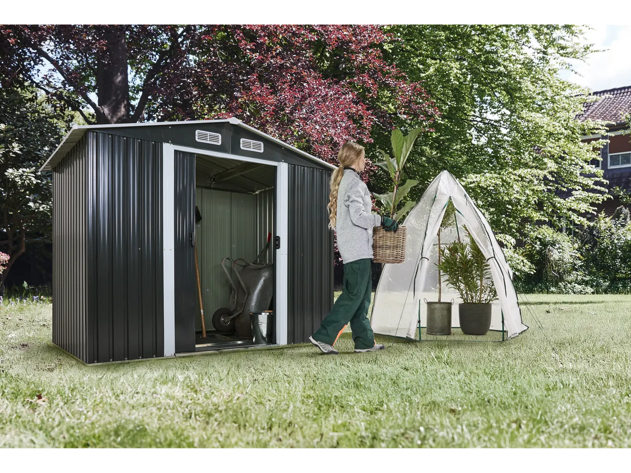 Woman by a garden shed and wintering tent with plants.